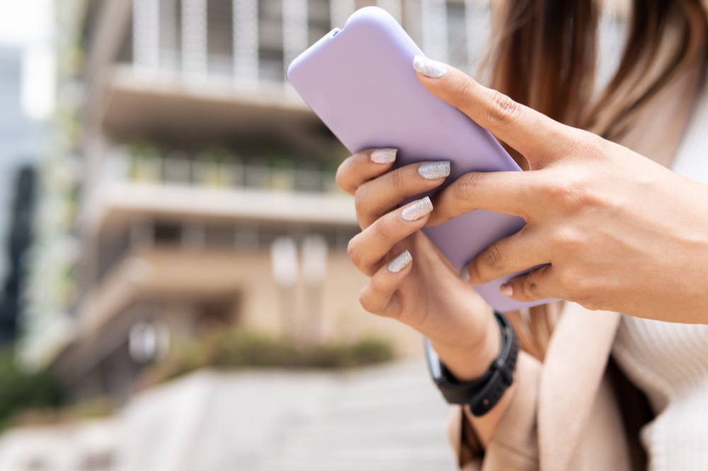 Hands with glittery nails using a smartphone outdoors