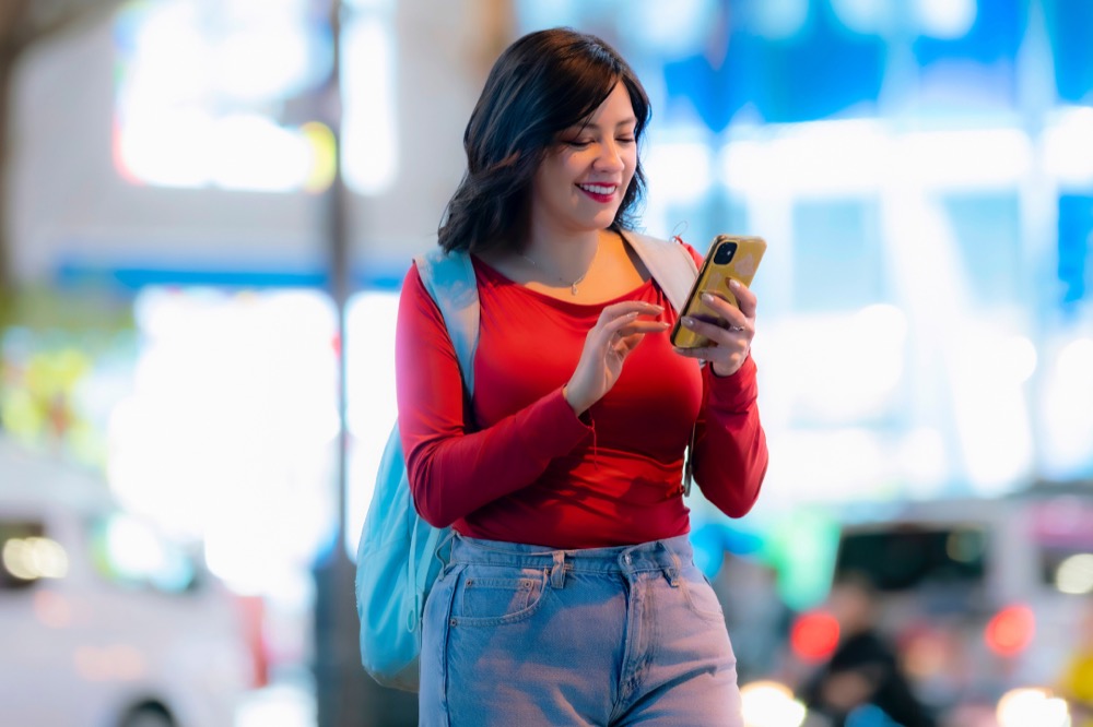 A smiling woman using a smartphone on a brightly lit city street